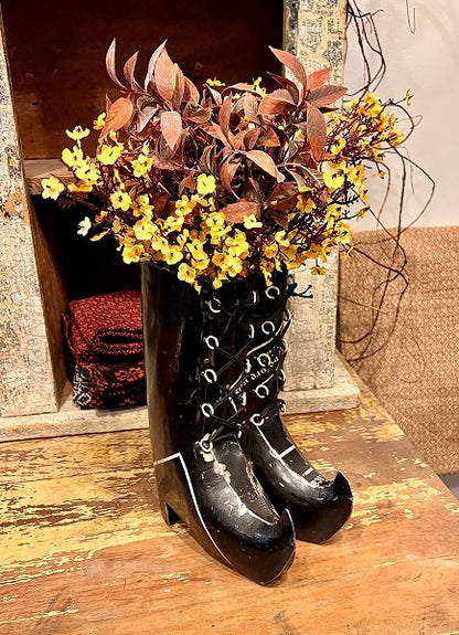 Decorative display of black lace-up boots with yellow flowers and red leaves.