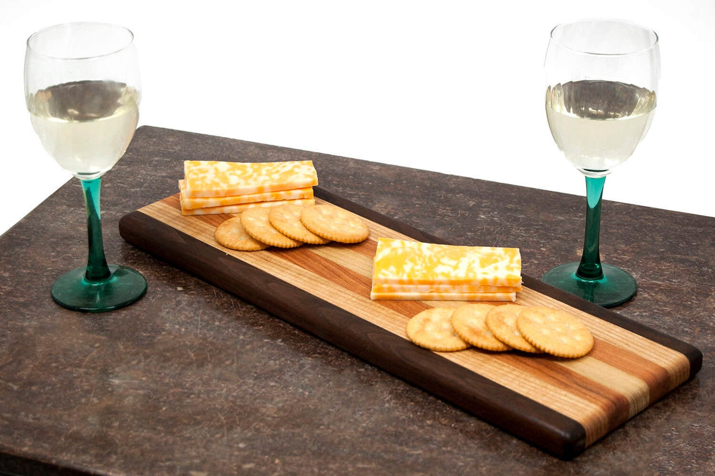 Wooden cheese board with crackers and cheese, accompanied by two wine glasses on a dark surface.