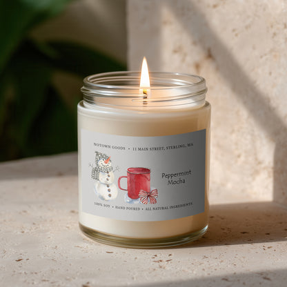 Clear jar candle with white wax and a decorative label on a blurred outdoor background.