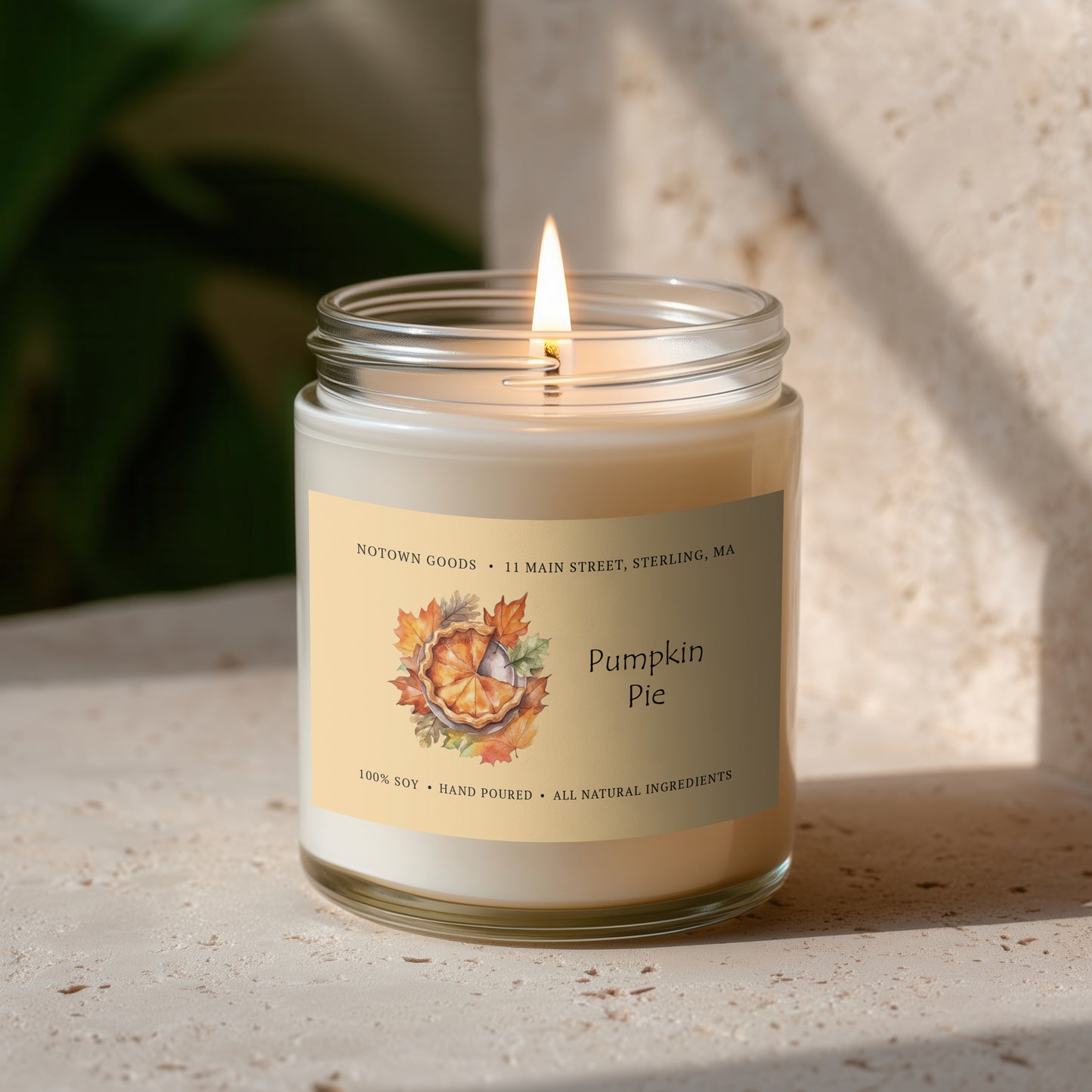 Clear jar candle with white wax and a decorative label on a blurred outdoor background.