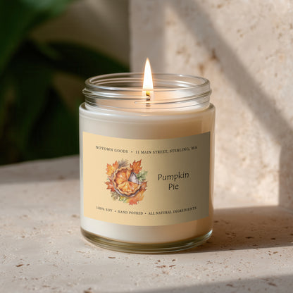 Clear jar candle with white wax and a decorative label on a blurred outdoor background.