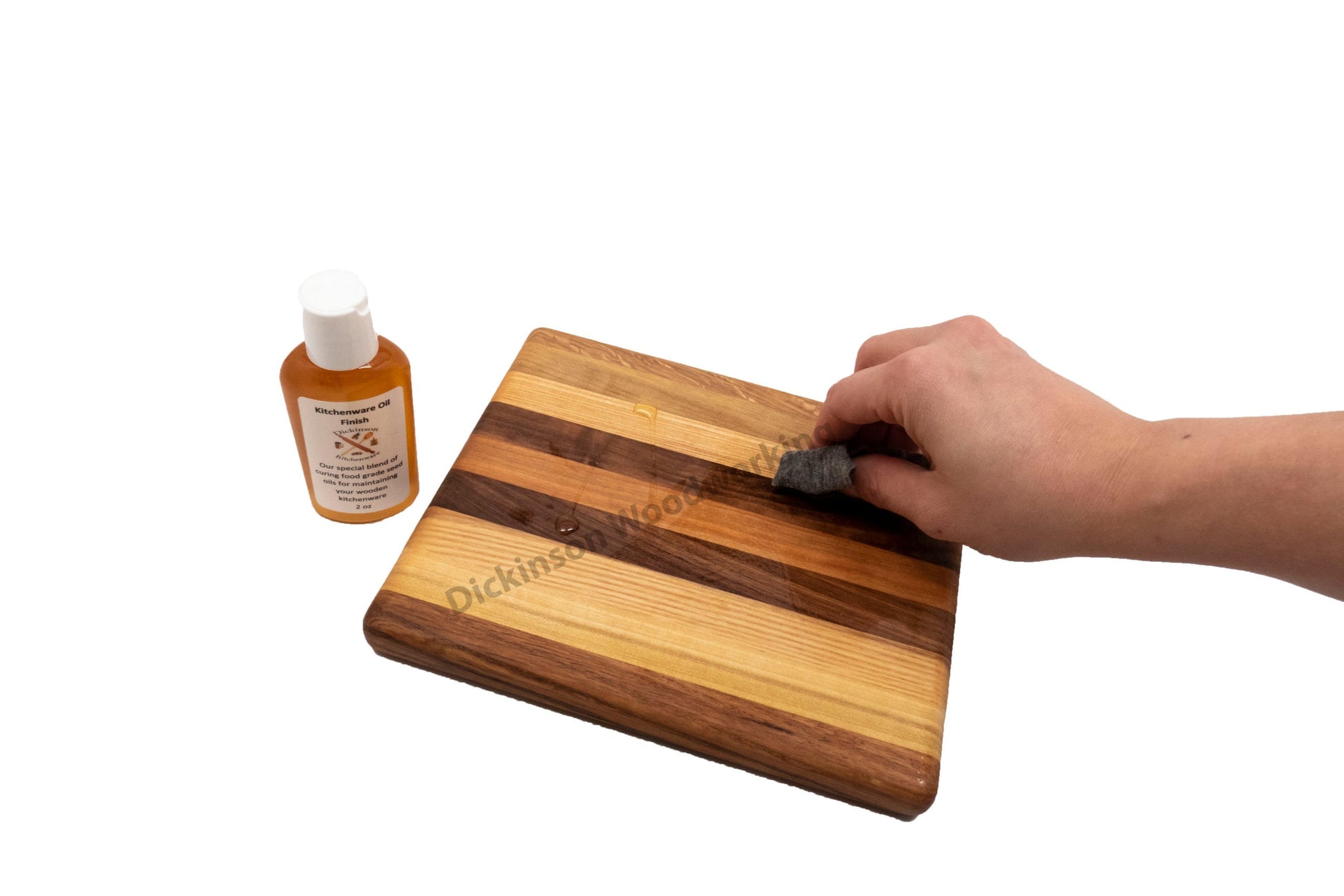 Person's hand applying a wood finish to a wooden cutting board with a bottle of finish next to it.