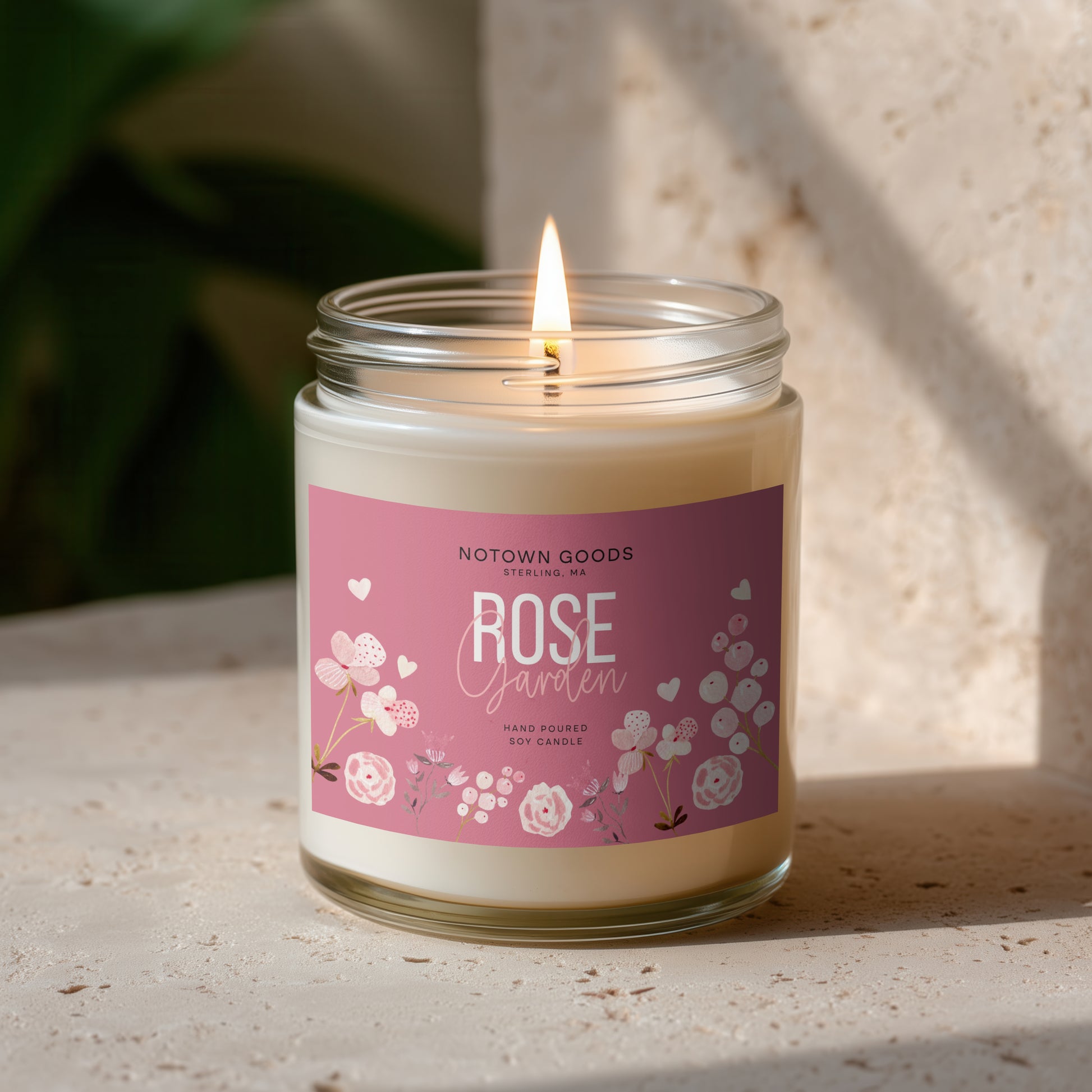 Clear jar candle with white wax and a decorative label on a blurred outdoor background.