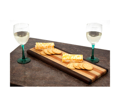 Wooden serving board with cheese and crackers, accompanied by two glasses of white wine on a dark surface.