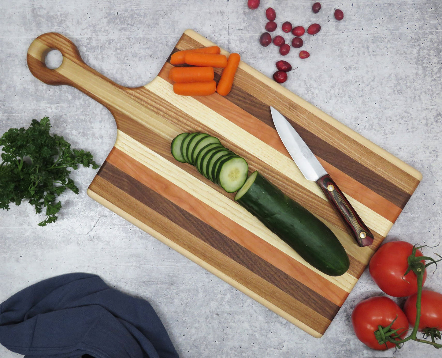 Wooden cutting board with sliced vegetables and a knife on a gray surface