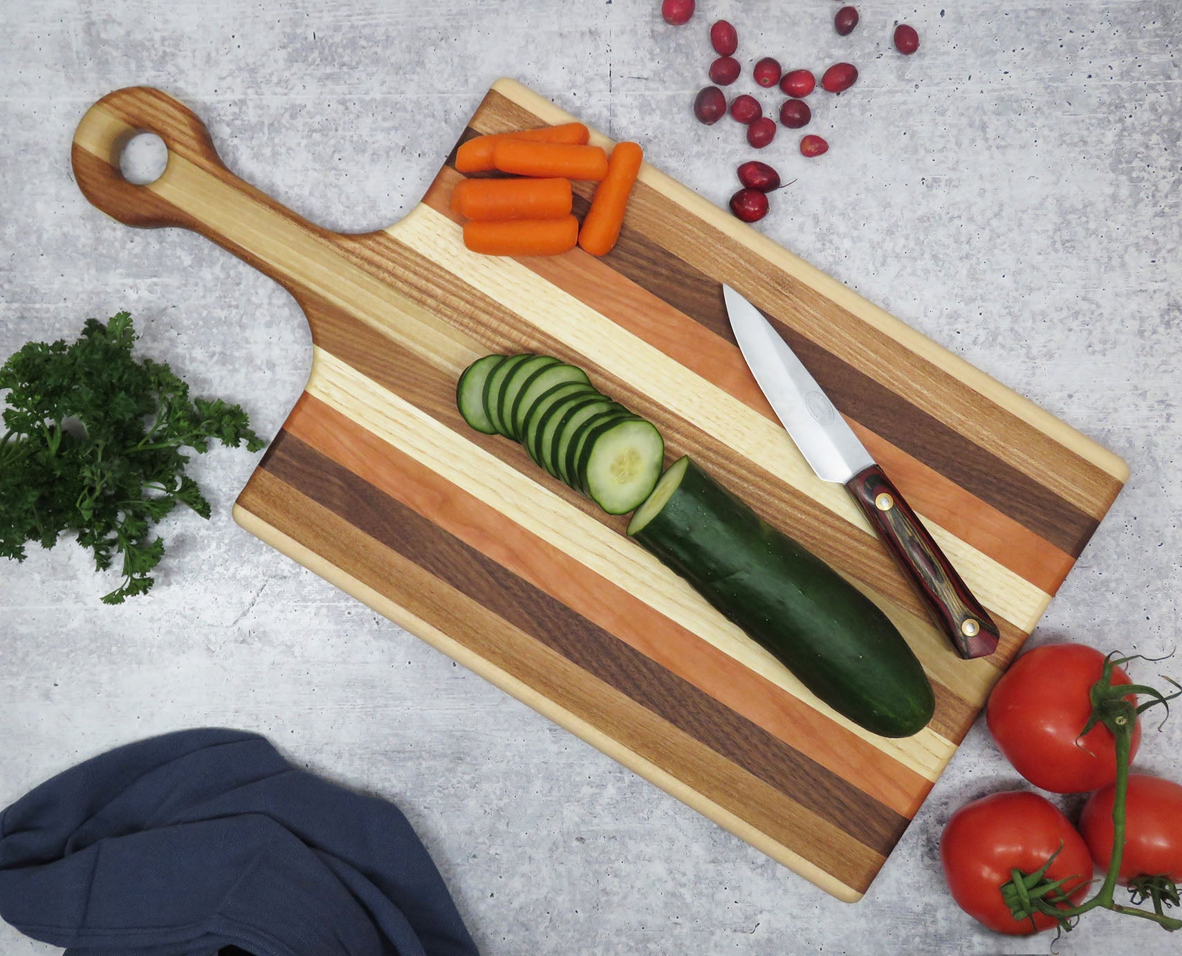 Wooden cutting board with sliced vegetables and a knife on a gray surface
