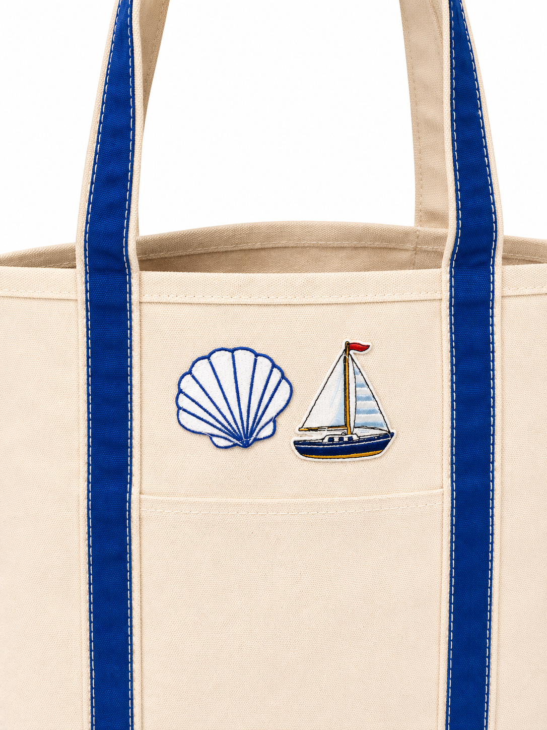 Beige tote bag with blue handles featuring a shell and sailboat design on a white background