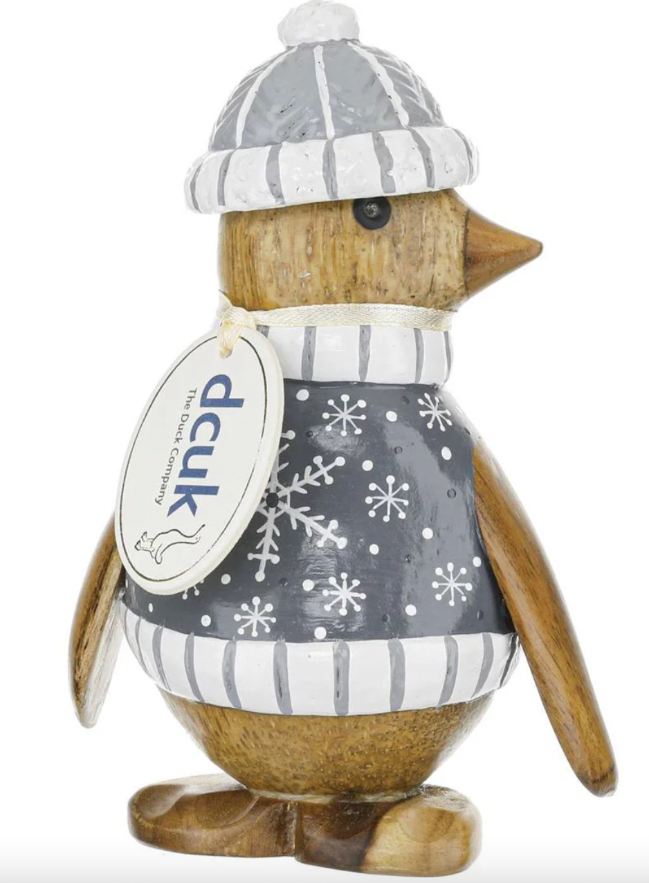 Wooden penguin figurine wearing a gray sweater with snowflake pattern and a striped hat on a white background.