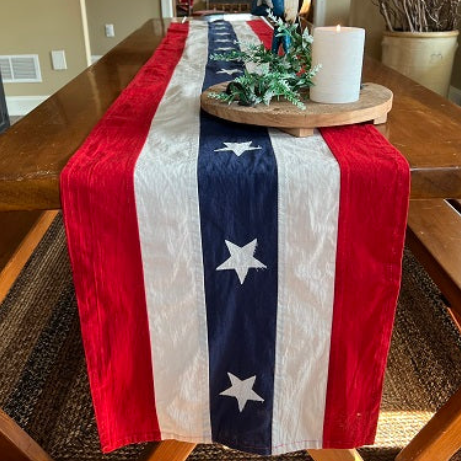 American flag table runner on a wooden table with a candle and greenery.