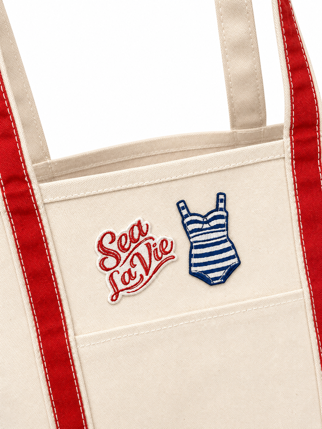 Beige tote bag with red straps featuring 'Sea La Vie' text and a swimsuit illustration.