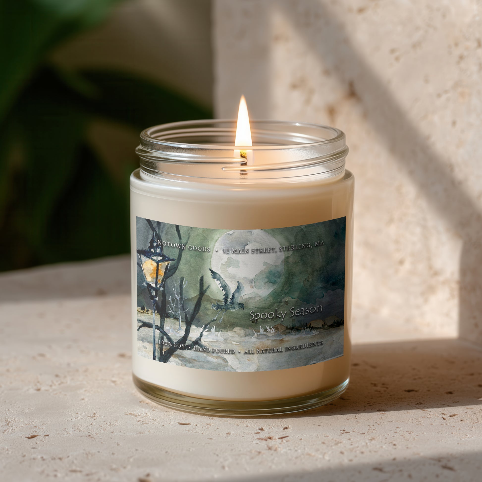 Clear jar candle with white wax and a decorative label on a blurred outdoor background.