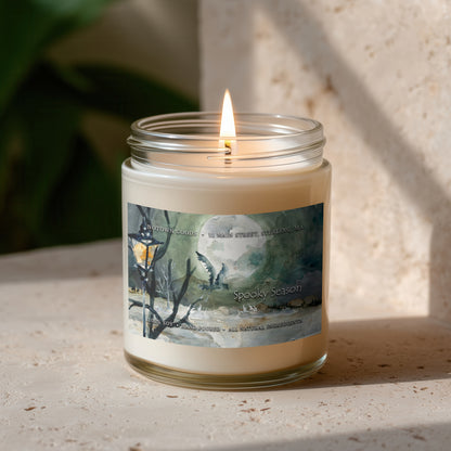 Clear jar candle with white wax and a decorative label on a blurred outdoor background.