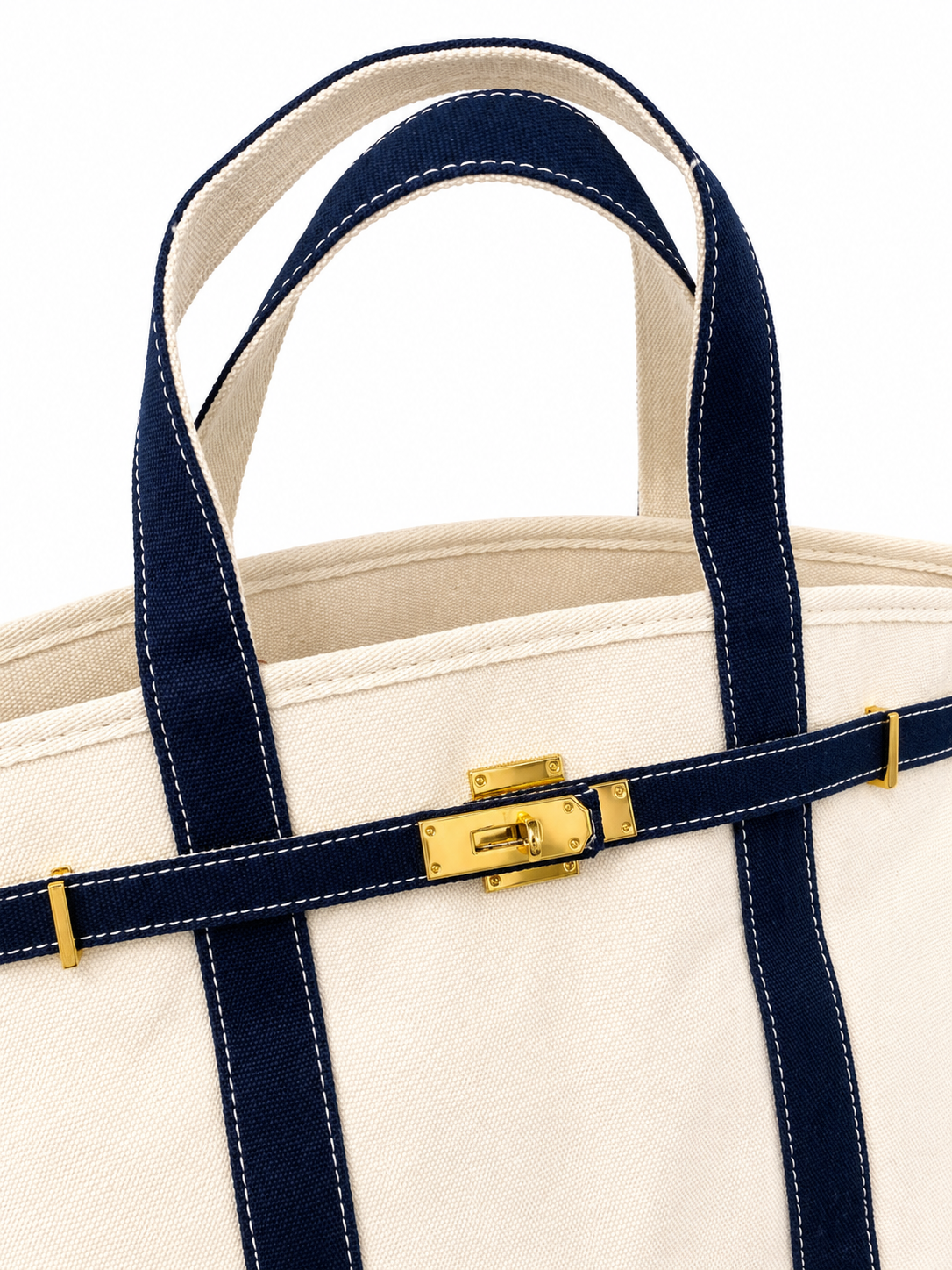 Close-up of a beige tote bag with navy straps and gold hardware on a white background
