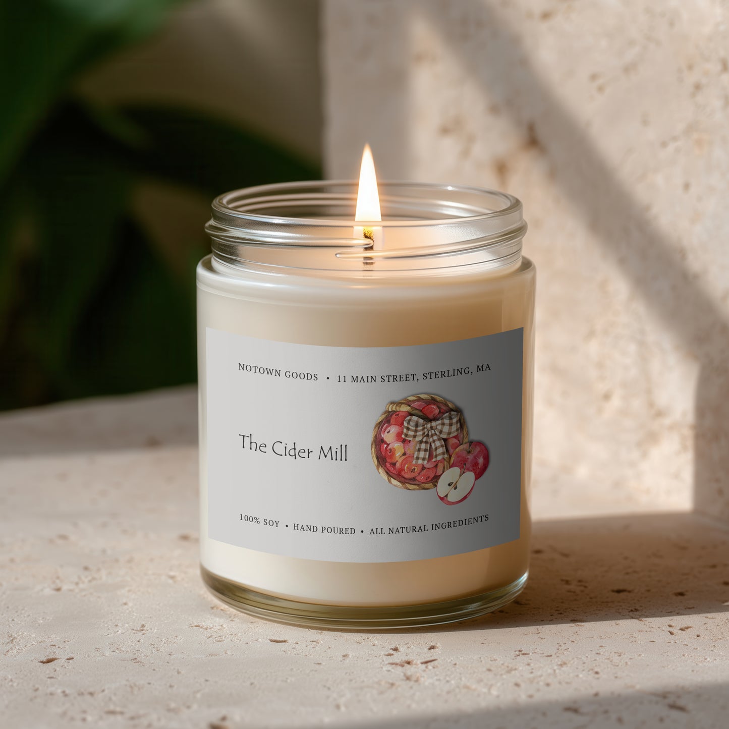 Clear jar candle with white wax and a decorative label on a blurred outdoor background.