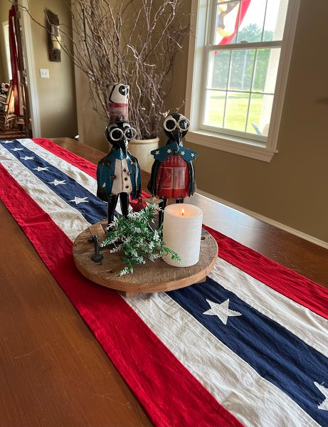 Decorative table setting with American flag runner, candles, and statues in a home interior.