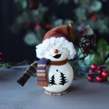 Decorative snowman figurine with a scarf and hat on a table with a blurred Christmas tree background.
