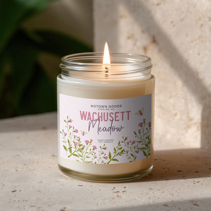 Clear jar candle with white wax and a decorative label on a blurred outdoor background.