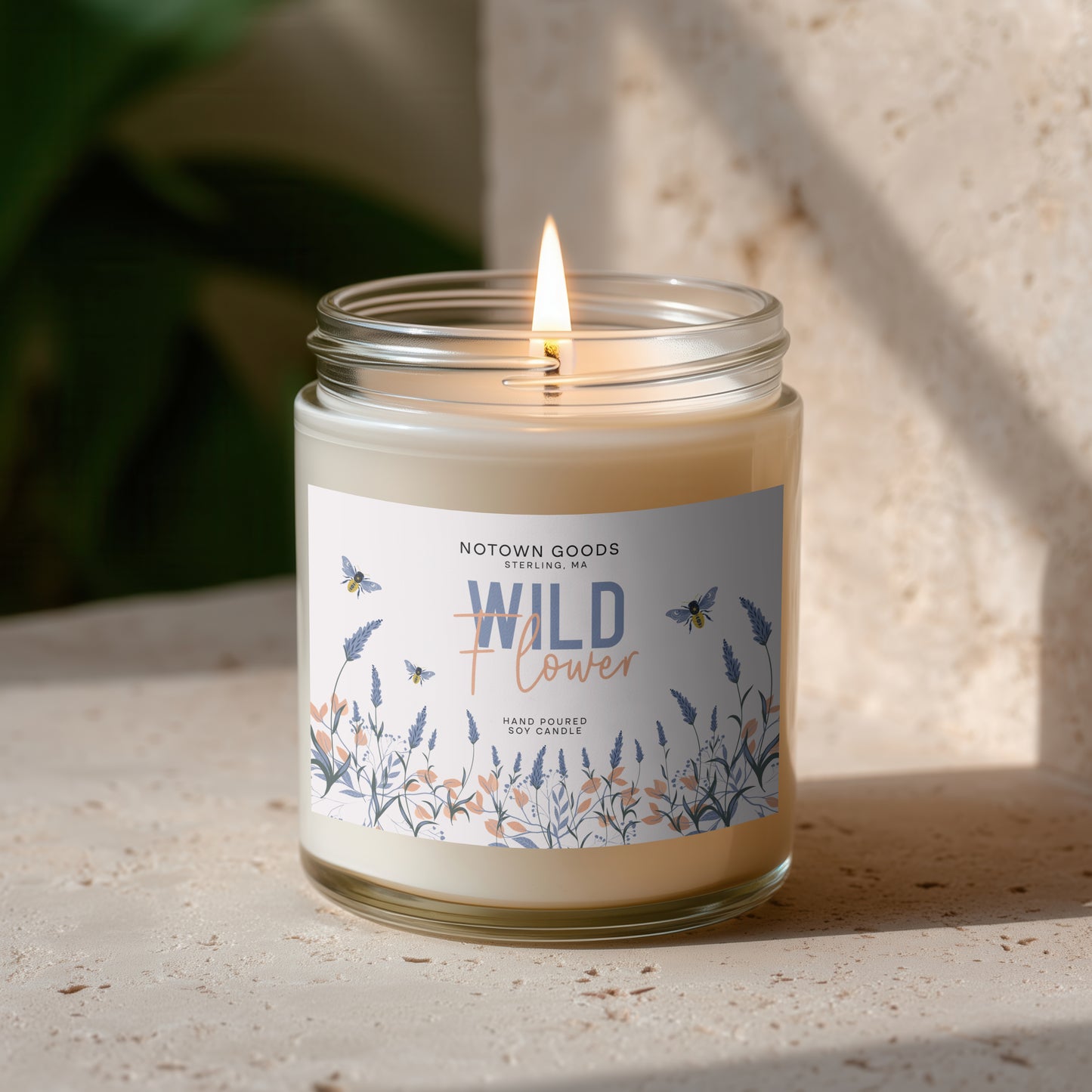 Clear jar candle with white wax and a decorative label on a textured outdoor background.