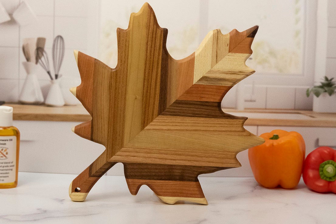 Wooden leaf-shaped cutting board on a kitchen counter with peppers in the background