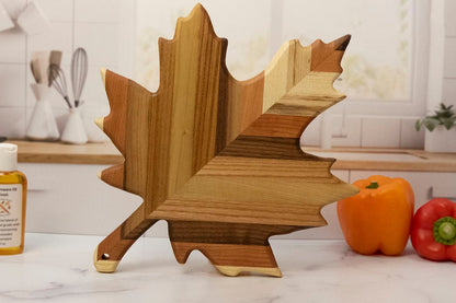 Wooden leaf-shaped cutting board on a kitchen counter with peppers in the background