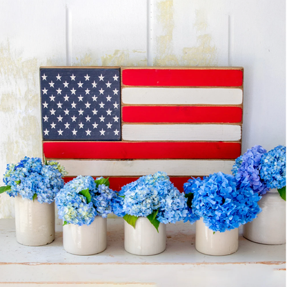 American flag decoration with blue flowers in white vases on a wooden surface.