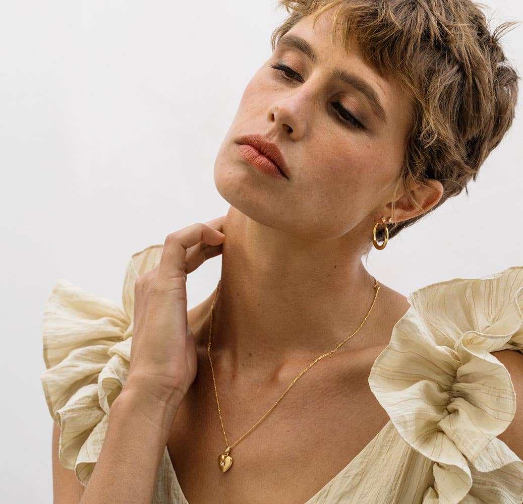 Woman wearing a gold necklace and earrings with a plain background