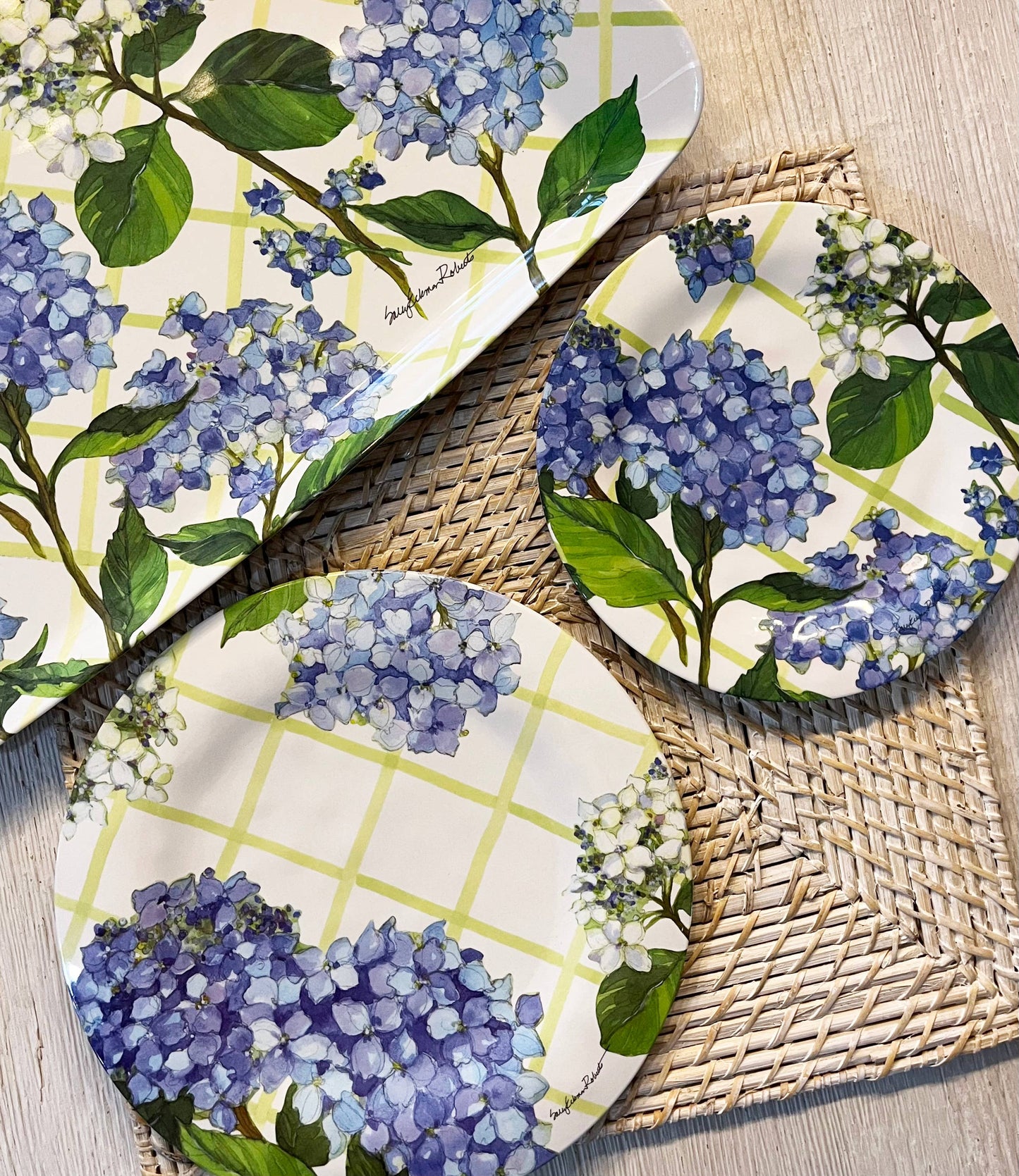 Set of three round plates with blue hydrangea floral design on a woven mat.