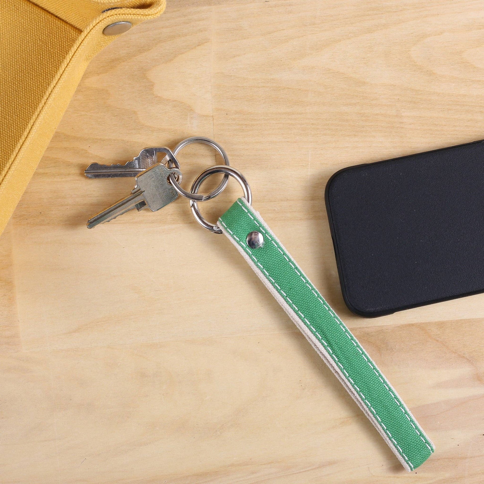 Green keychain with keys on a wooden surface next to a phone