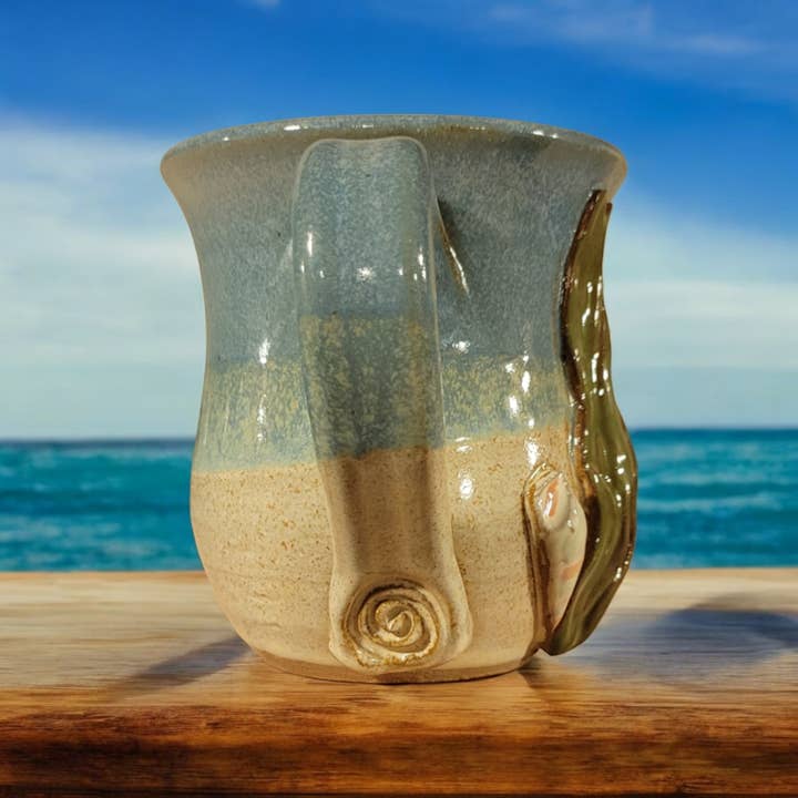 Ceramic mug with sand-like texture on a wooden surface with ocean view