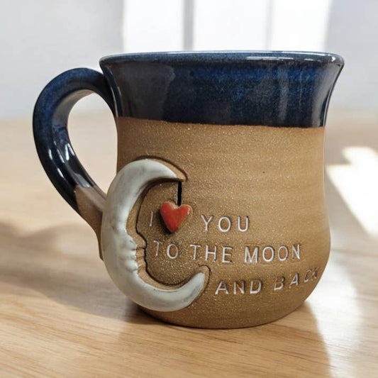 Ceramic mug with moon and heart design and 'I love you to the moon and back' text on a wooden surface.