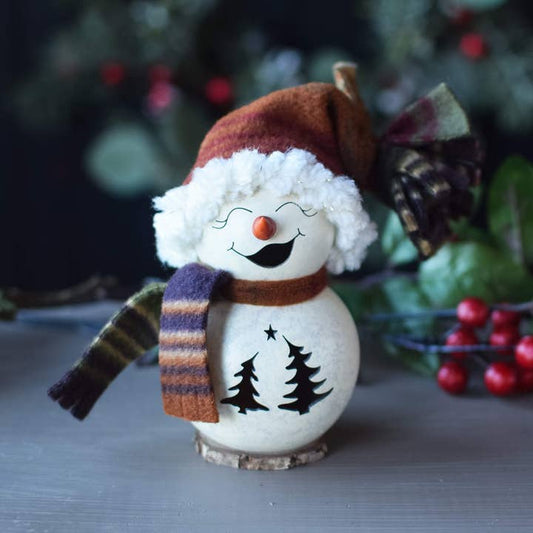 Decorative snowman figurine with a striped scarf and tree design, set against a blurred green and red background.
