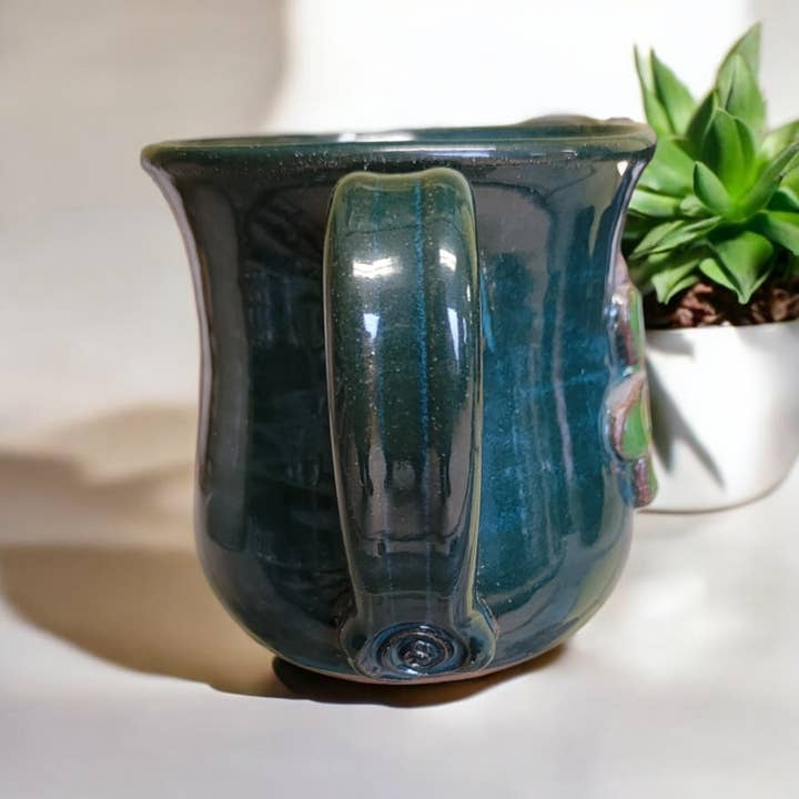 Blue ceramic mug on a white surface with a plant in the background
