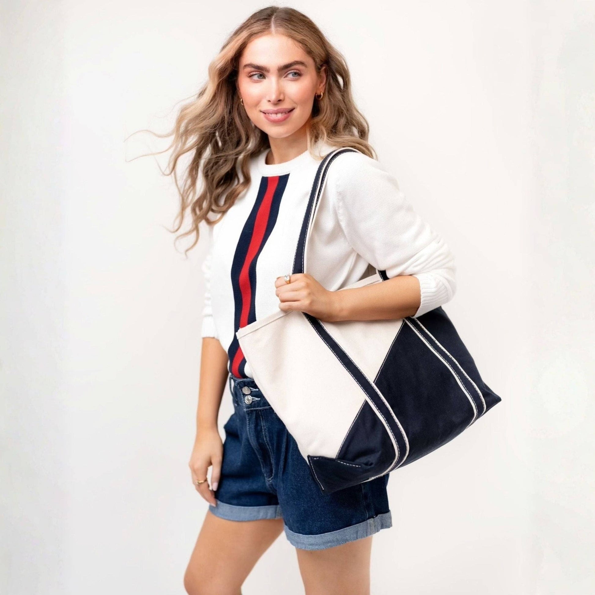 Woman holding a navy tote bag with white accents against a plain background