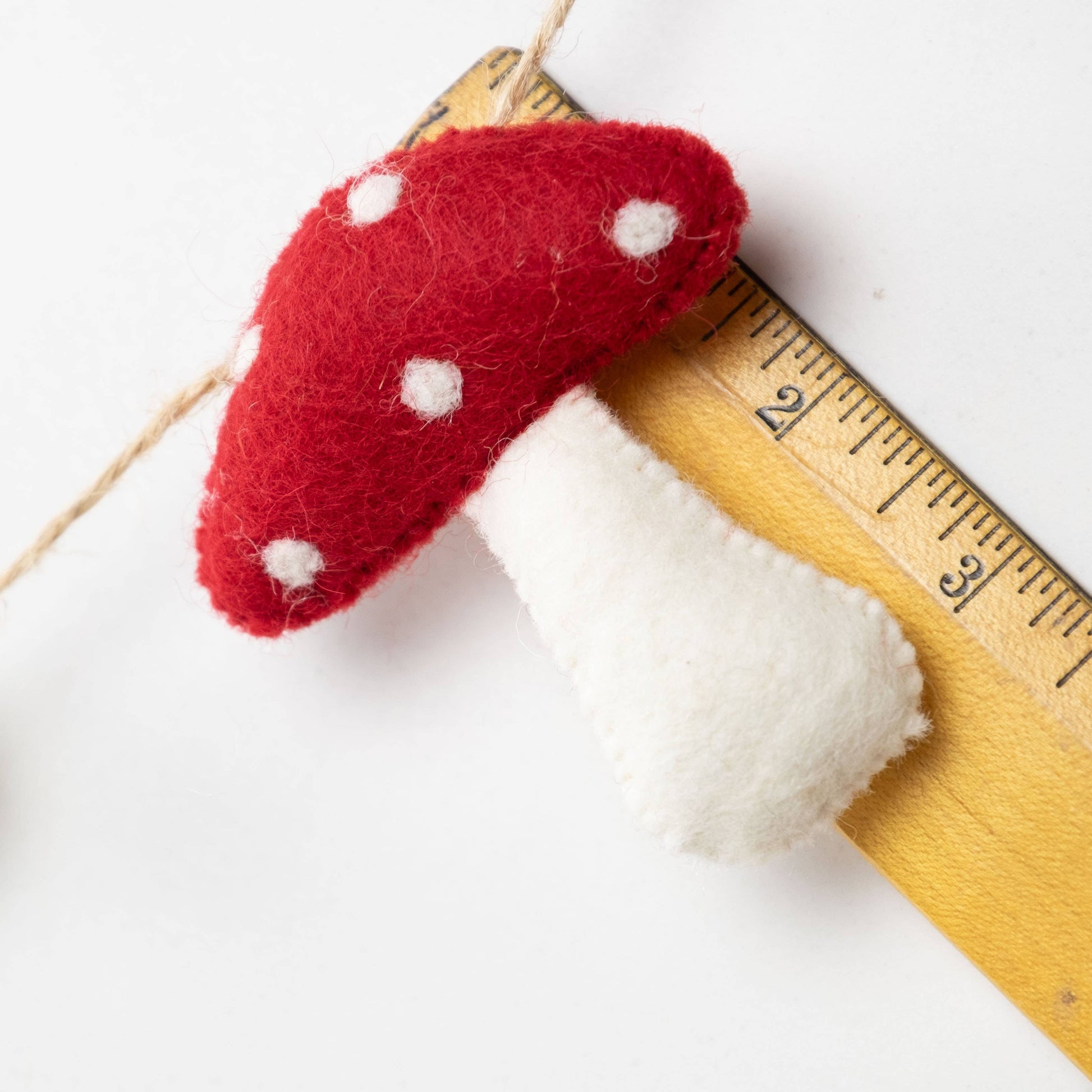 Felted red mushroom with white spots on a wooden ruler against a white background