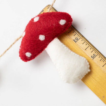 Felted red mushroom with white spots on a wooden ruler against a white background