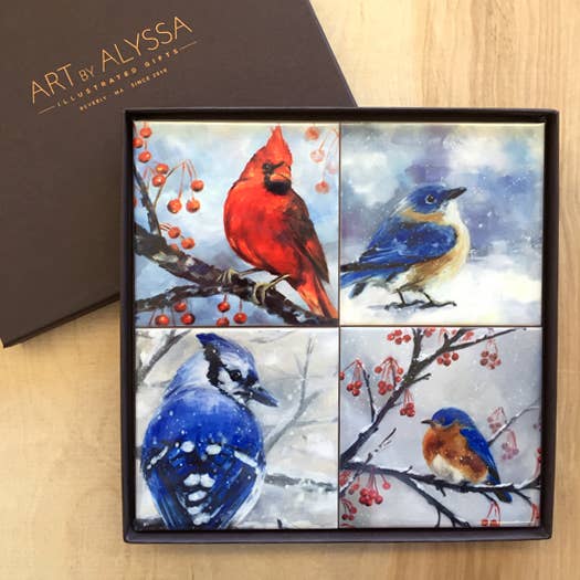 Four coasters with birds on branches with berries in a gift box on a wooden background.