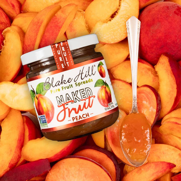 Jar of Blake Hill Naked Fruit Peach Spread surrounded by sliced peaches and a spoonful of peach spread.