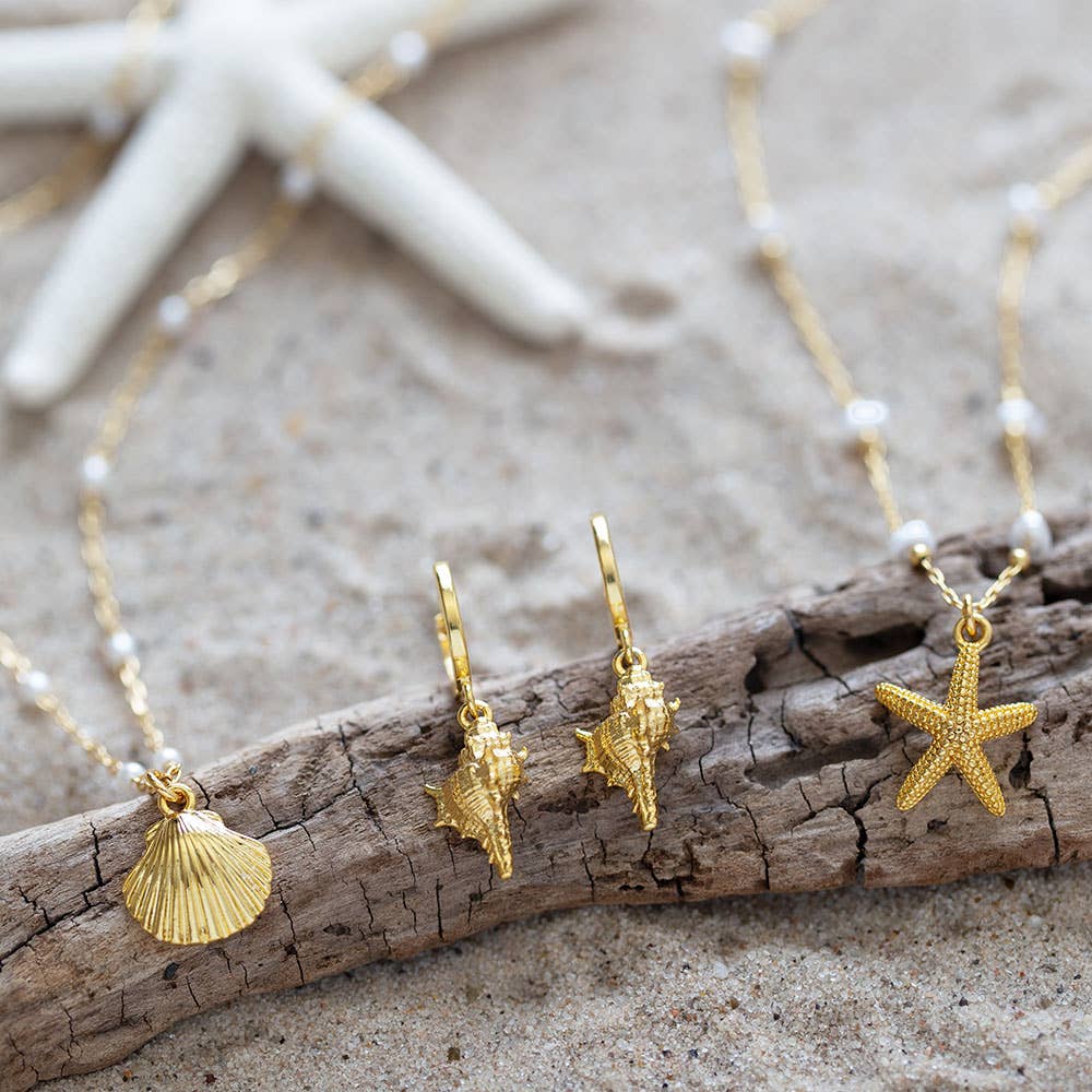 Gold jewelry with shell and starfish charms on a wooden branch and sand background