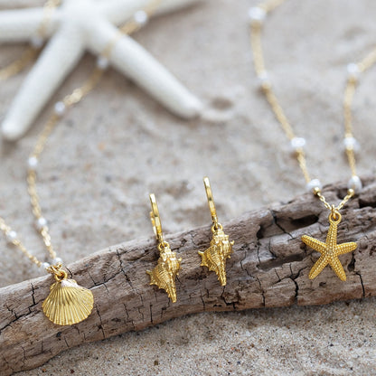 Gold jewelry with shell and starfish charms on a wooden branch and sand background