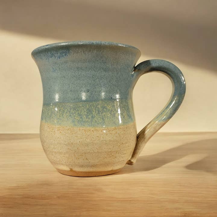 Ceramic mug with blue and beige glaze on a wooden surface