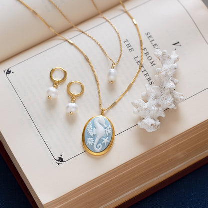 Gold necklace with a blue pendant and earrings on an open book with coral.