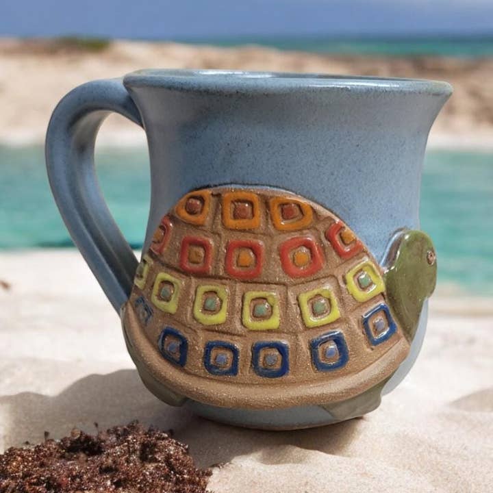 Ceramic mug with turtle design on a sandy beach