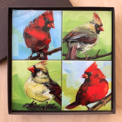 Four coasters with painted cardinals in a gift box on a wooden surface.
