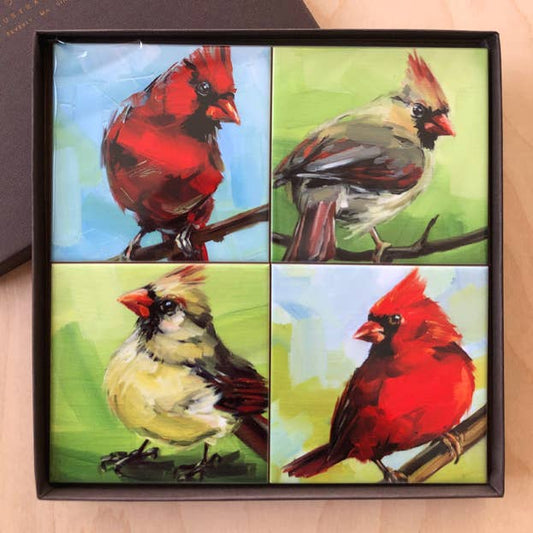 Four coasters with painted cardinals in a gift box on a wooden surface.