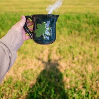Hand holding a mug with a clover design outdoors