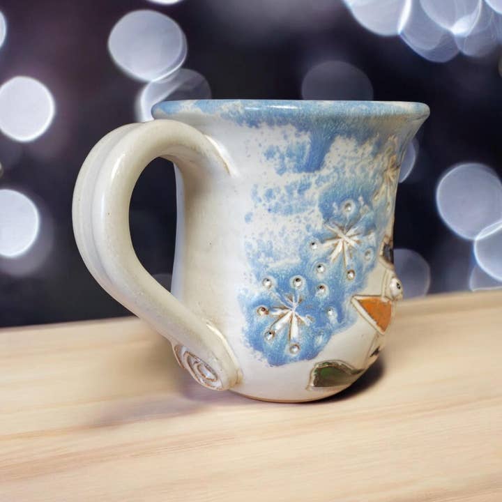 Ceramic mug with snowman design on a wooden surface with blurred lights in the background