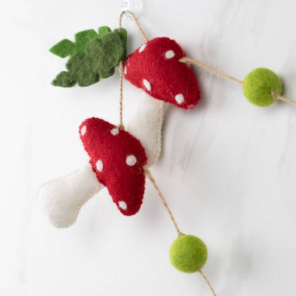 Felt mushroom garland with green leaves and pom-pom balls on a white background