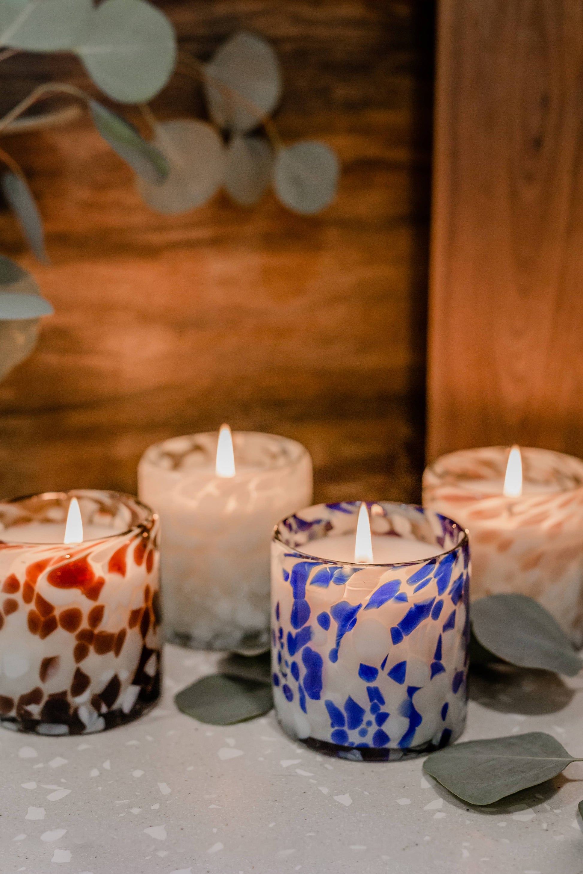Decorative candles with marbled patterns on a wooden surface with eucalyptus leaves.