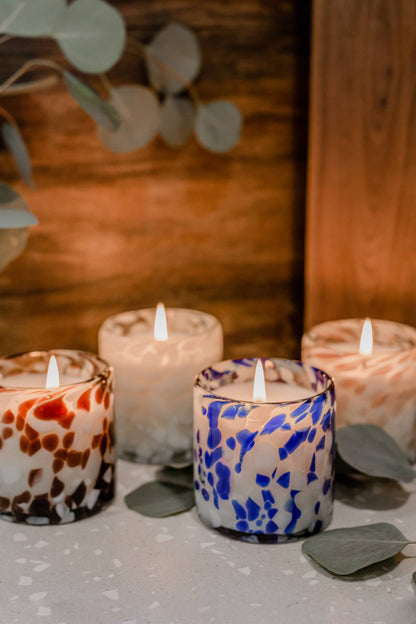 Decorative candles with marbled patterns on a wooden surface with eucalyptus leaves.