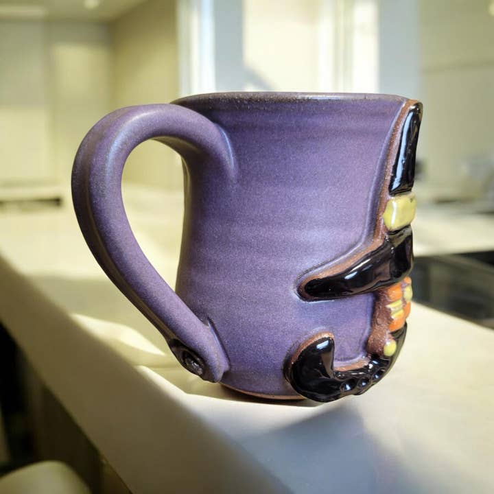Purple mug with a witch design on a kitchen counter. All images associated with this product listing show the same mug from various angles. The design is only on one side of the mug.